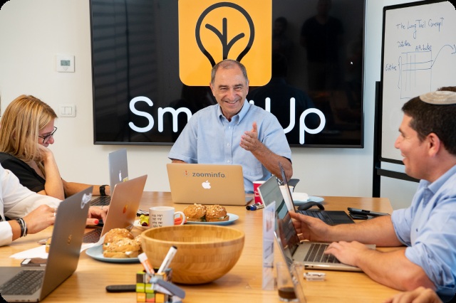 Yonatan Stern and colleagues around a meeting table at SmartUp, with laptops and a long-tail diagram on a whiteboard