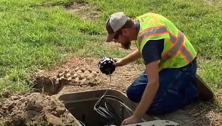 A fiber technician in a reflective vest working at an open underground utility enclosure