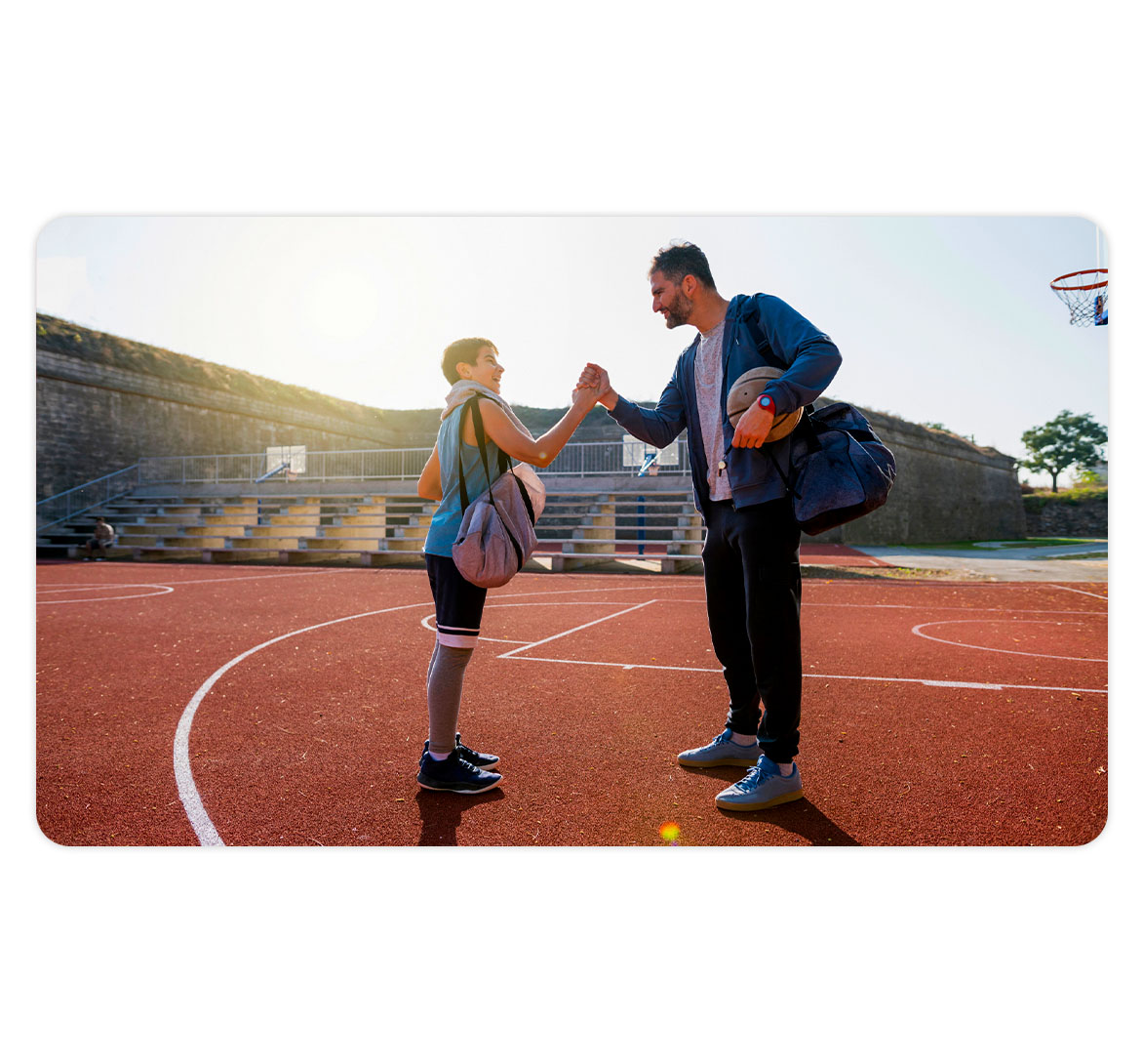 Promotional photograph of a coach and young basketball player greeting one another on an outdoor court