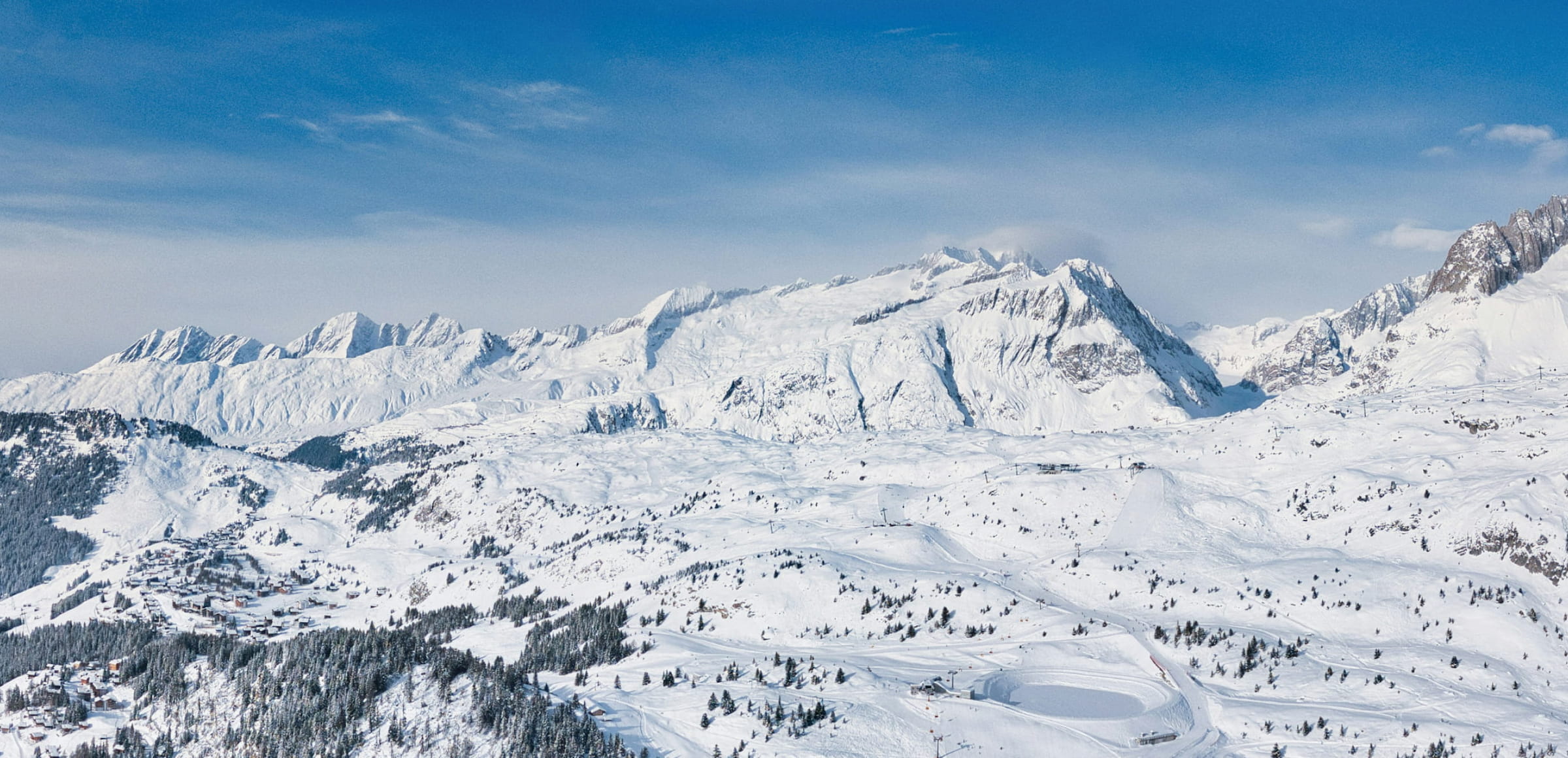 Snow-covered mountain slopes, forest and a resort village beneath a blue sky