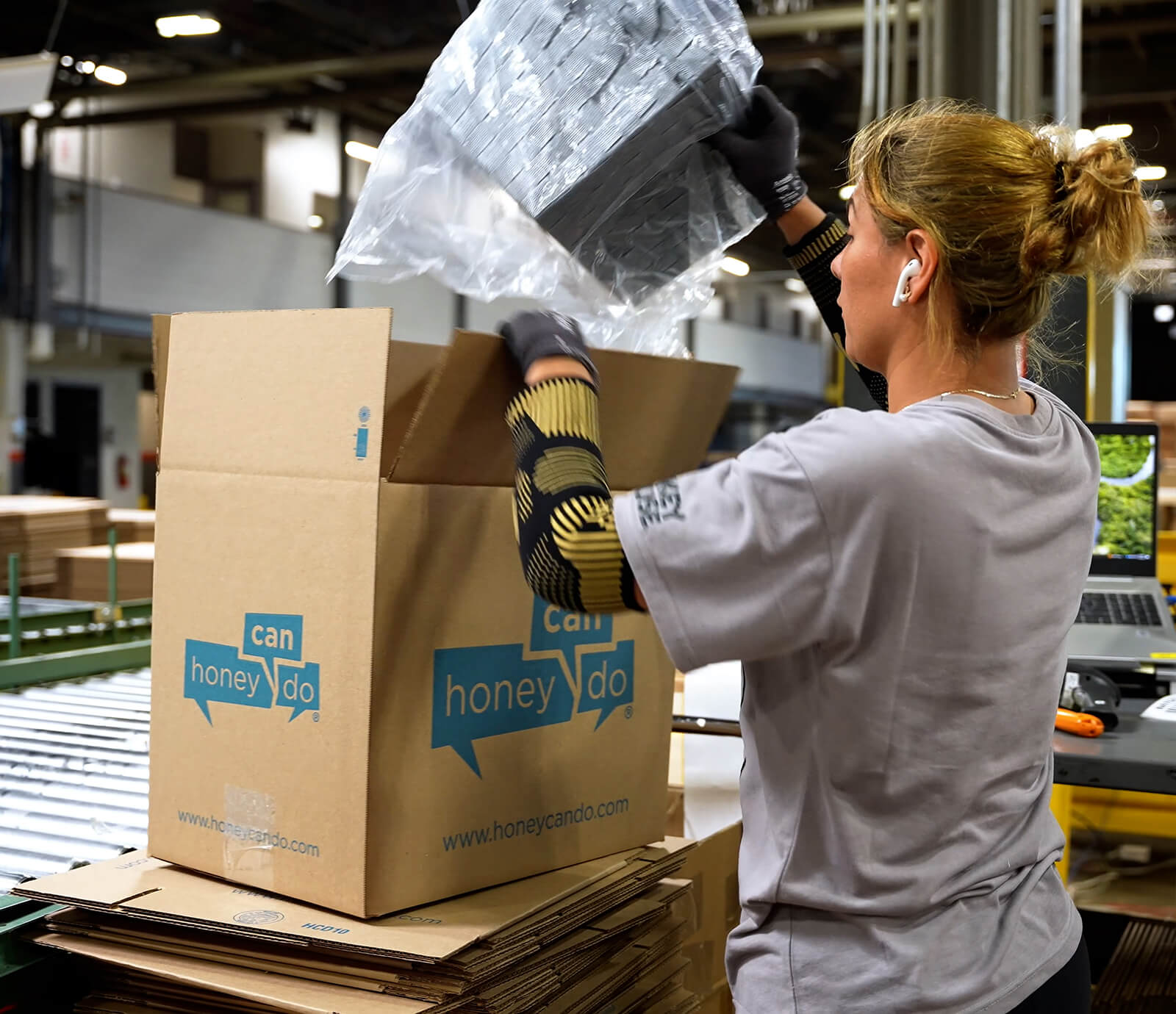 A Honey-Can-Do warehouse worker packs a large carton at a work station
