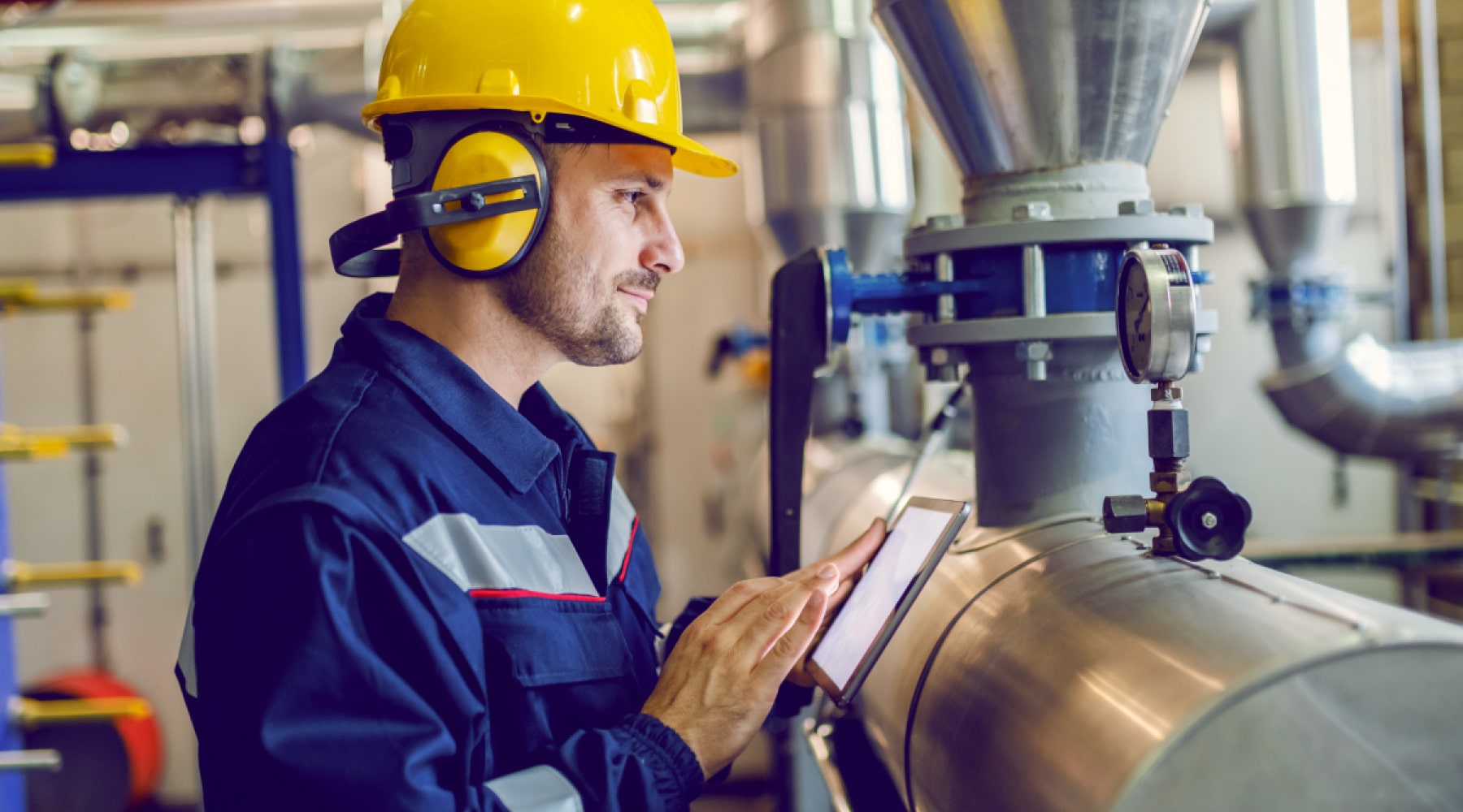 Maintenance technician using a tablet beside industrial pipes