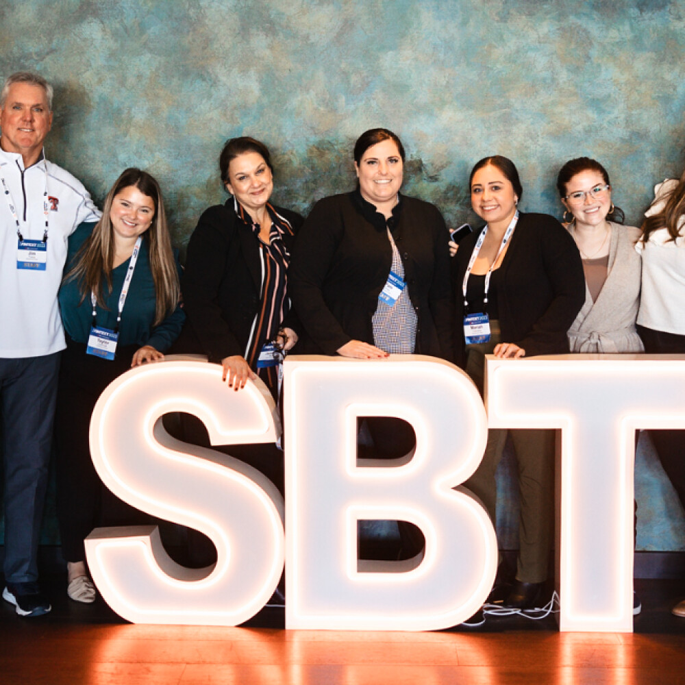 Solutions by Text team members gathered behind illuminated SBT letters