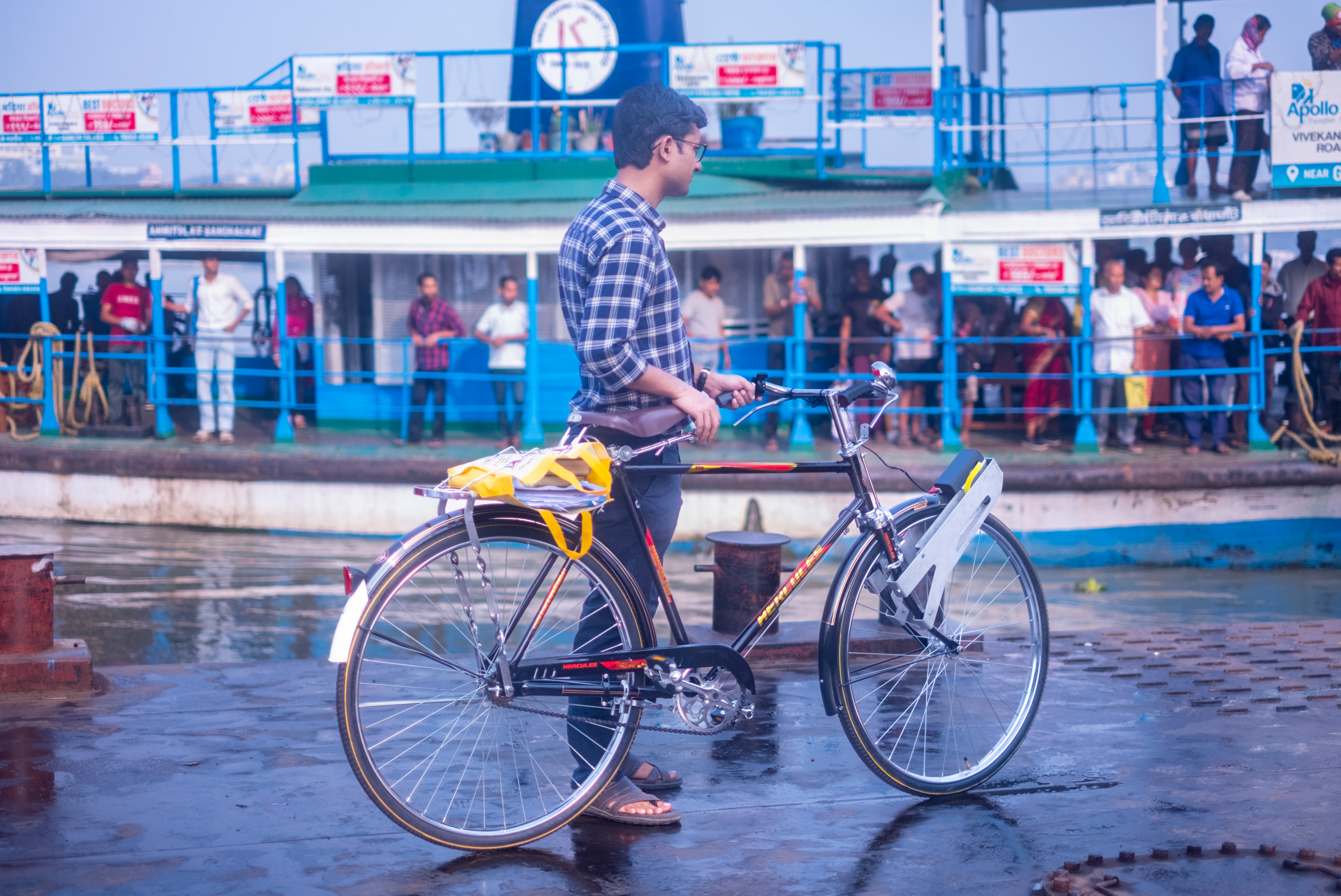 A person walks a black bicycle equipped with a BOLT front-wheel motor beside a ferry landing