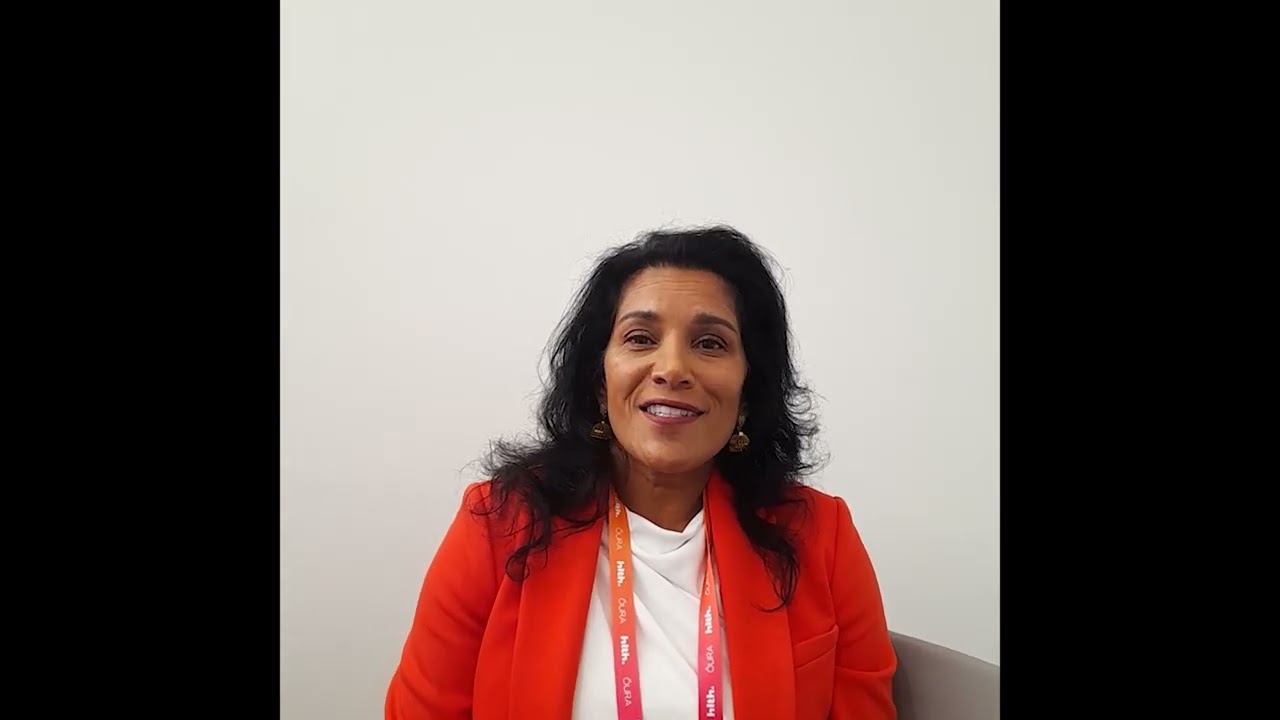 Sonia Millsom speaking in a 2023 video interview, wearing an orange jacket and event lanyard