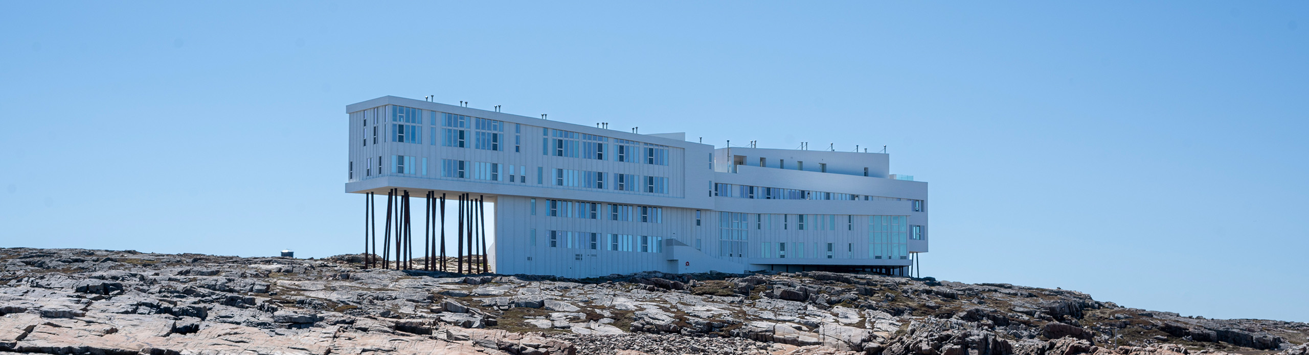 Fogo Island Inn extending across a rocky shoreline beneath a clear blue sky