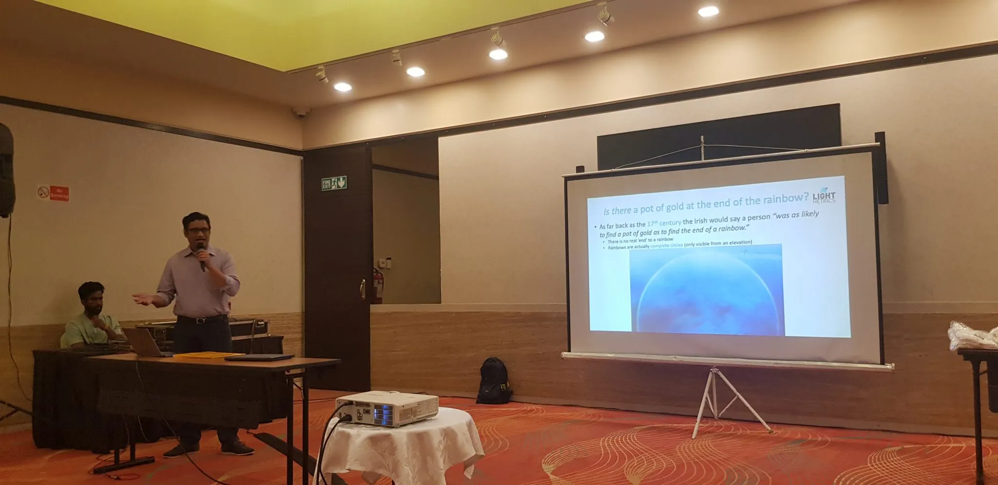 Soumik Ukil speaking beside a rainbow presentation slide at the LightMetrics team offsite in South Goa