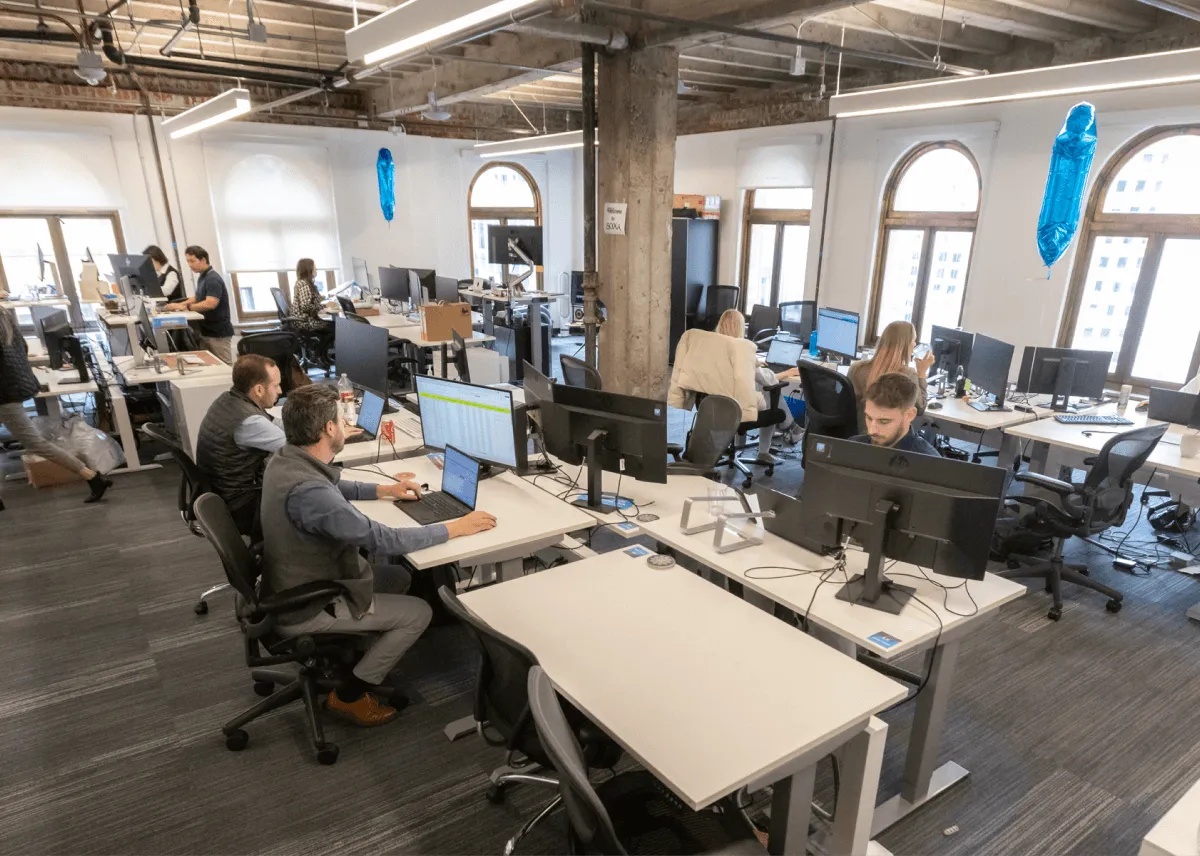 Sourcescrub office with employees working at shared desks and multiple monitors