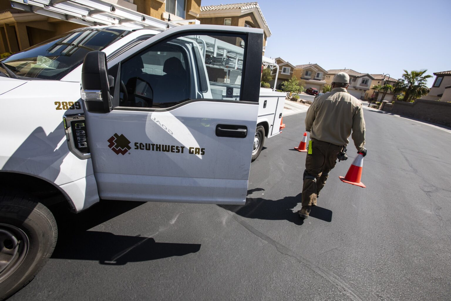 Southwest Gas technician carrying traffic cones beside a service truck on a Las Vegas residential street.