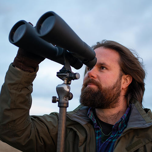 Space.com editor Jase Parnell-Brookes looking through large Celestron binoculars