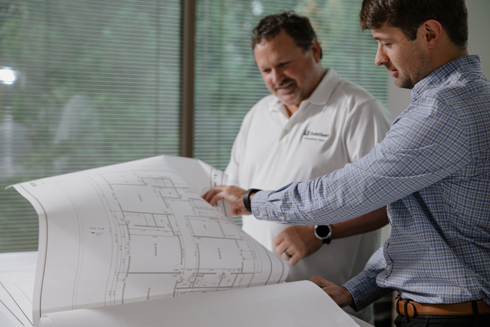 Two people reviewing a large set of building plans in a company-published photograph