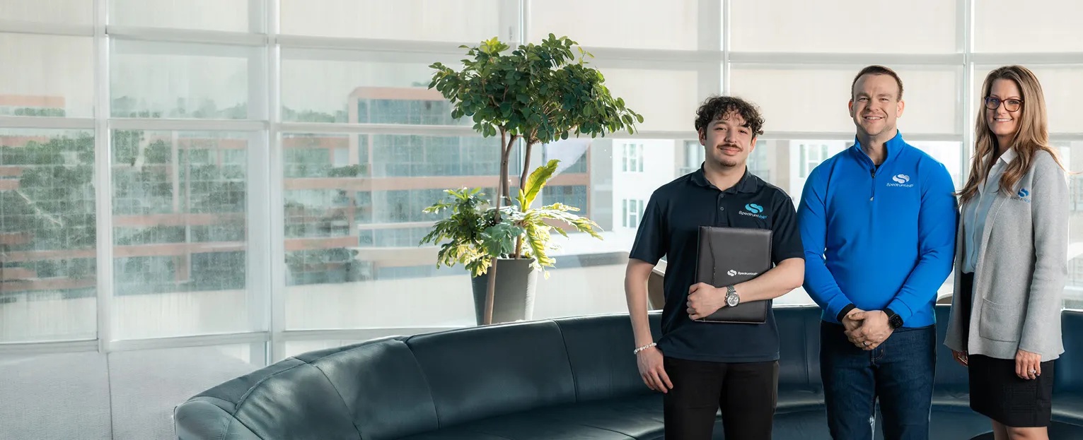 Three SpectrumVoIP team members standing beside a sofa in a bright office