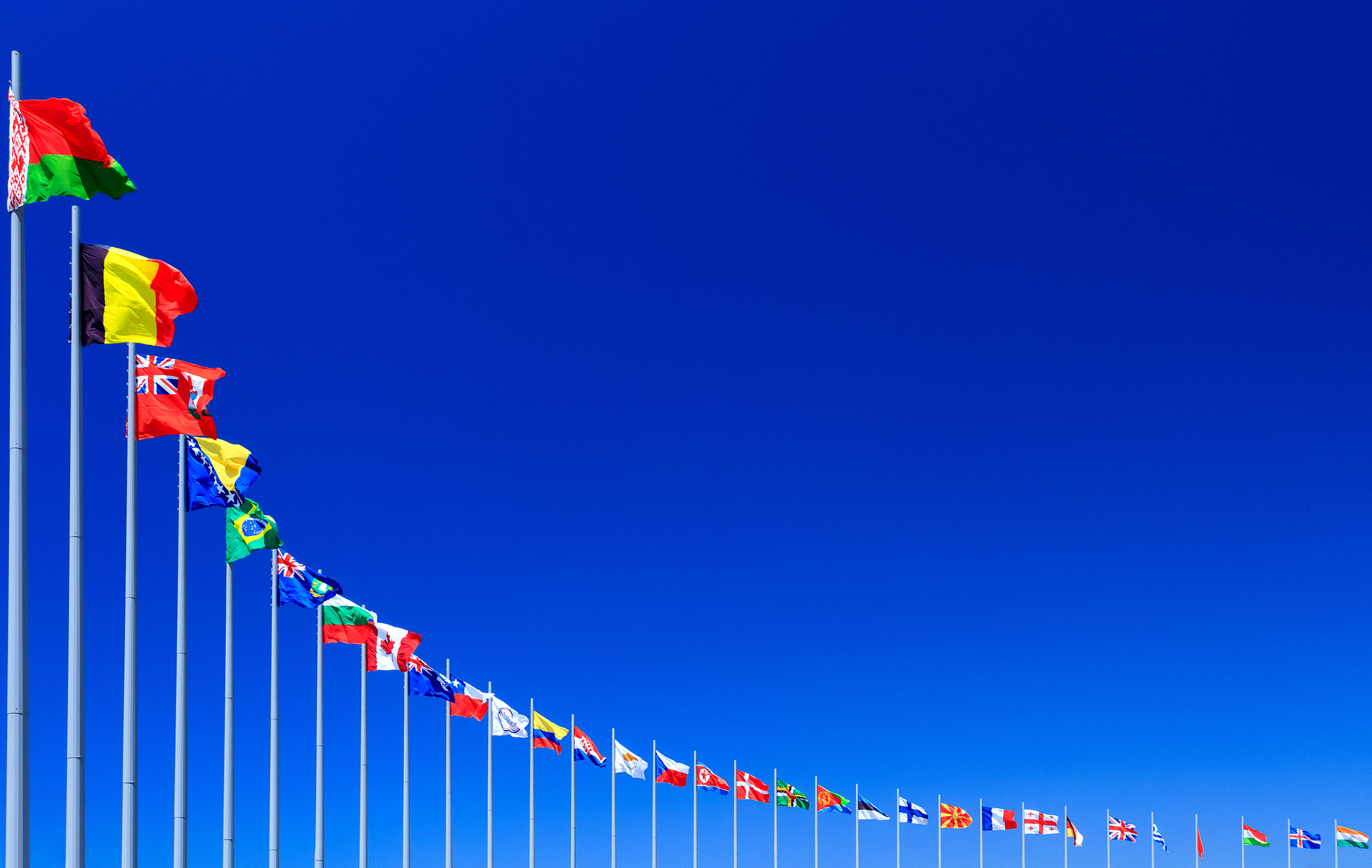 A line of international flags beneath a deep blue sky