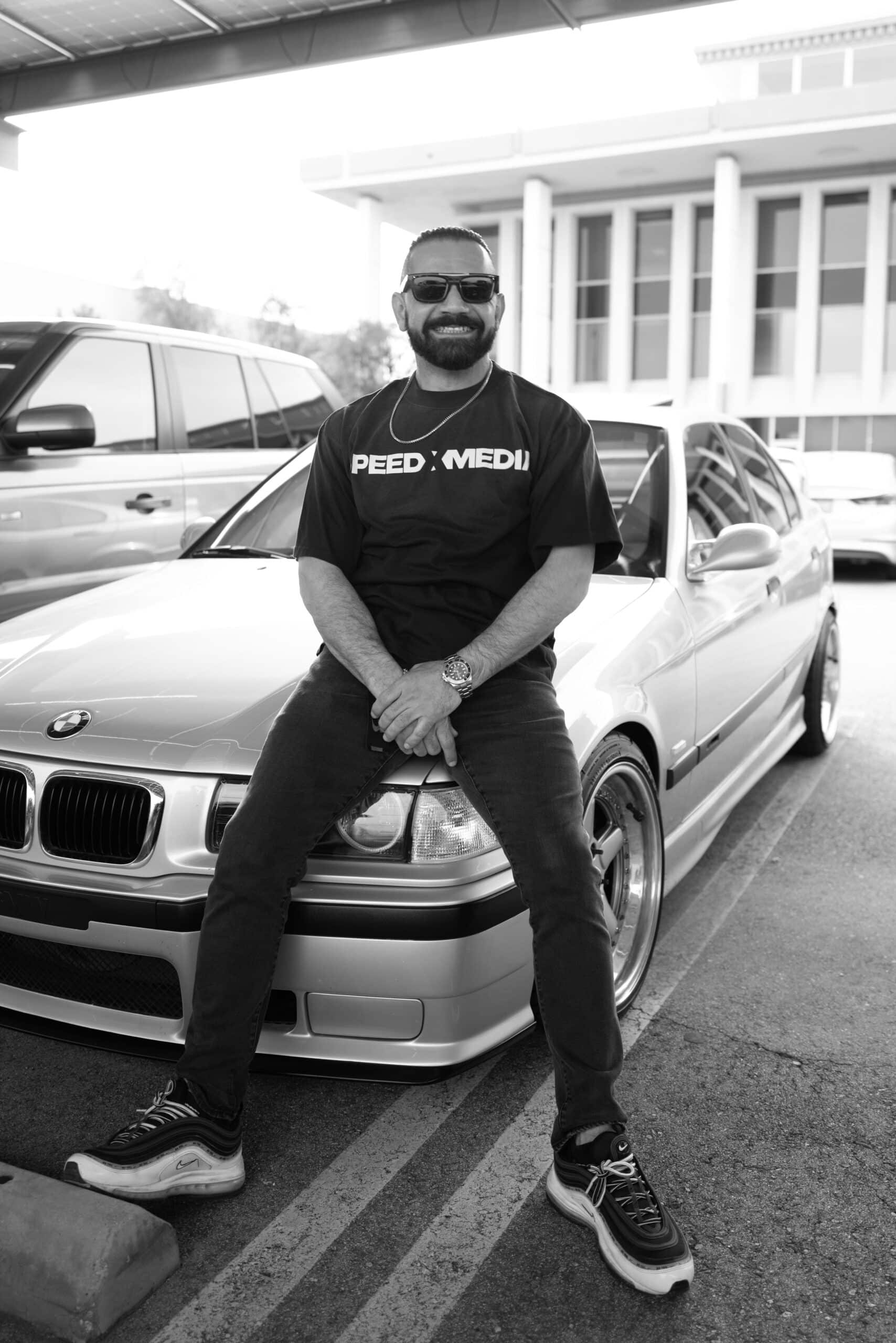 Dave, identified by SPEEDXMEDIA as creative director and founder, sitting on a silver car