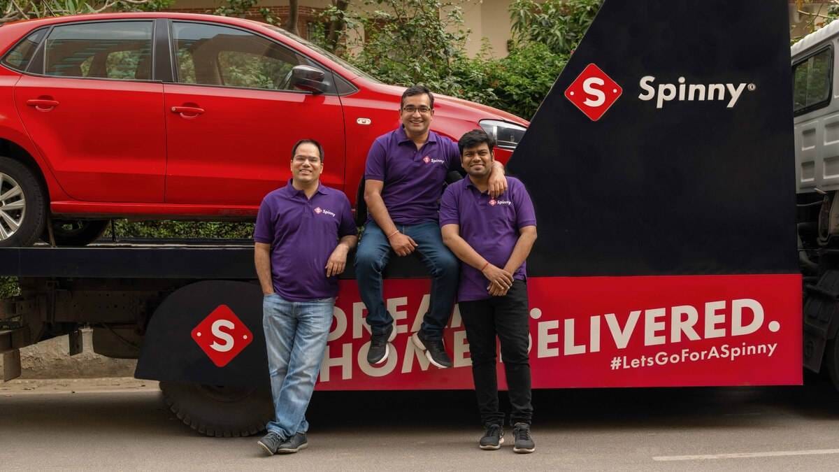 Three Spinny founders beside a delivery truck carrying a red hatchback