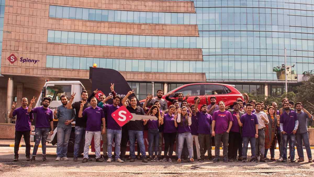 An early Spinny team posing outside an office with a delivery truck and oversized key