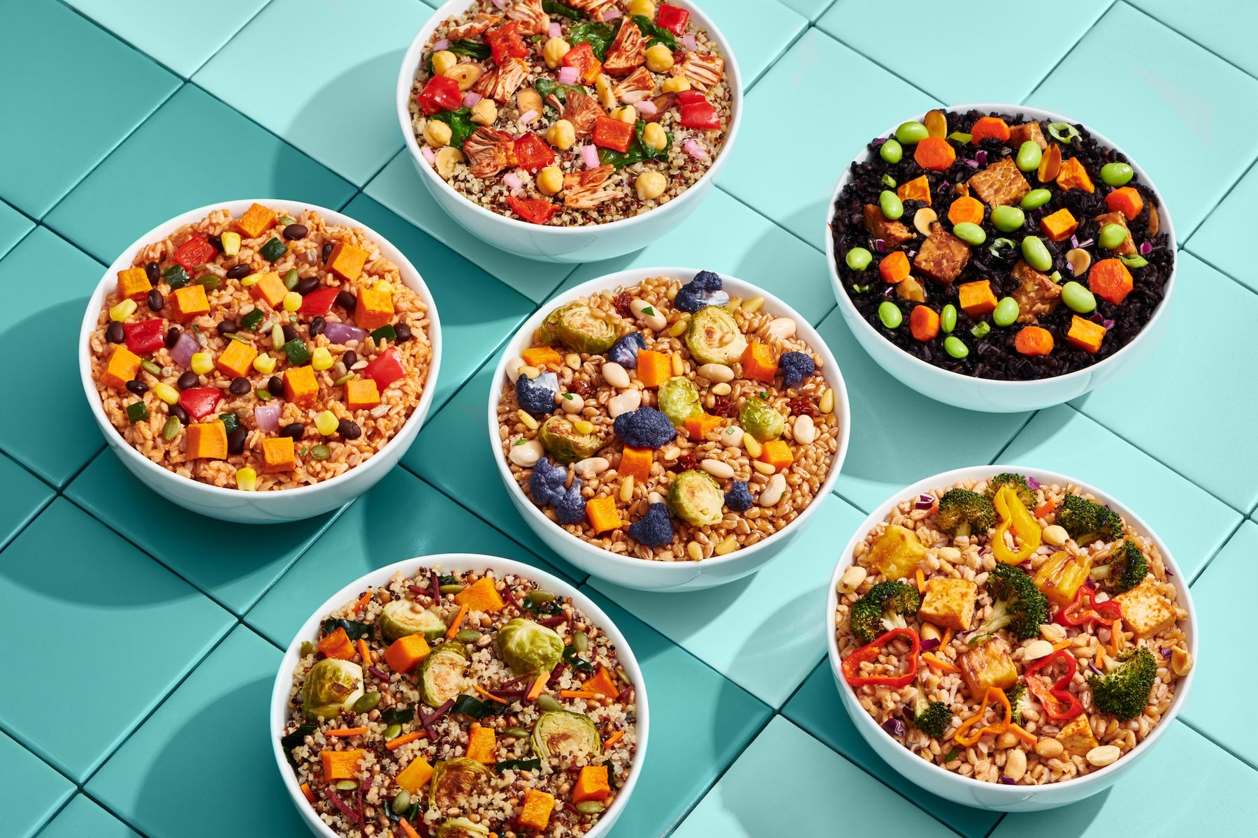 Six colorful plant-based bowls on a turquoise tiled surface