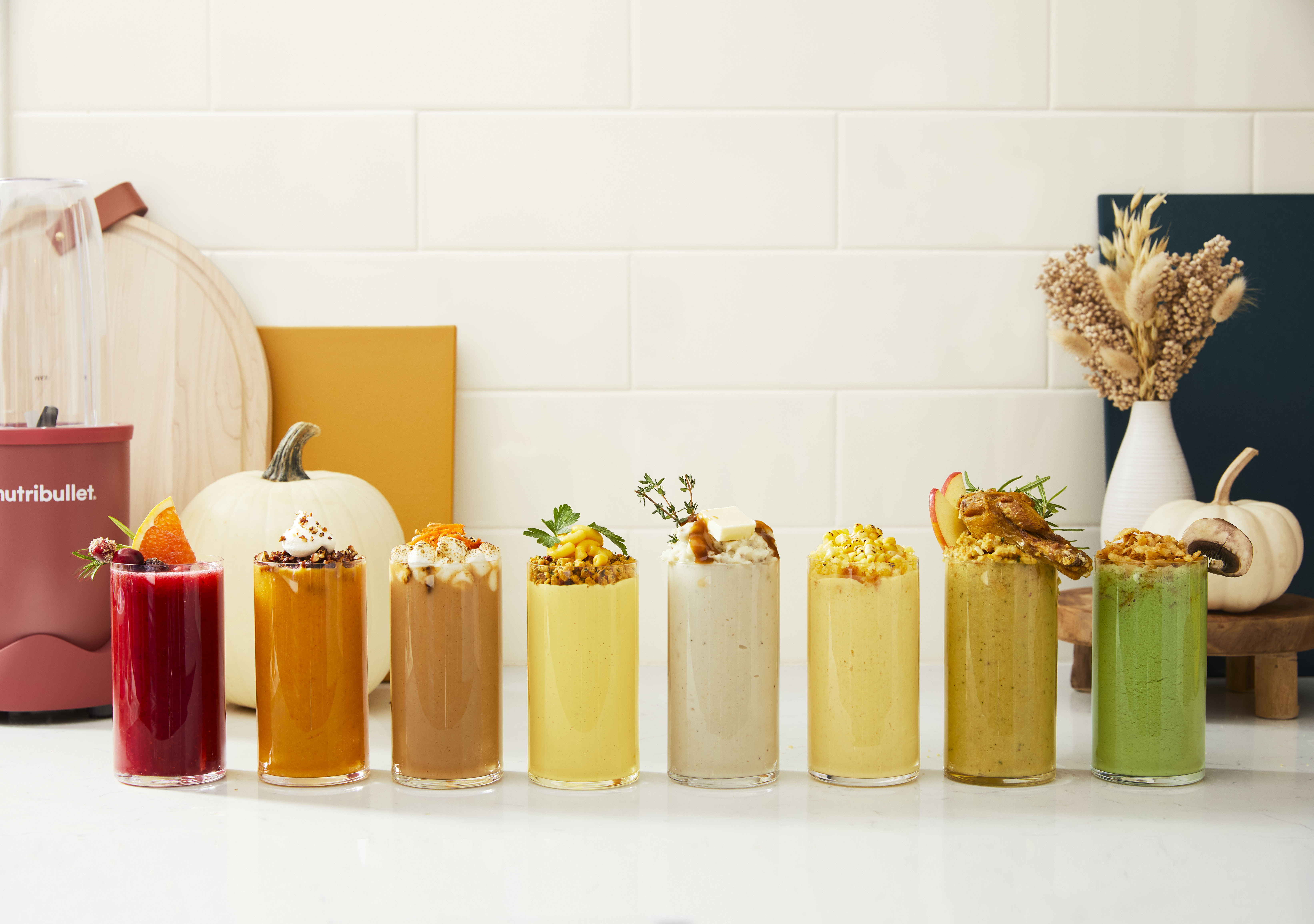 A row of colorful Thanksgiving side-dish smoothies beside a nutribullet blender