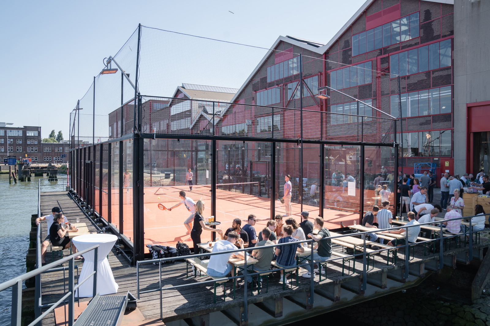 A portable padel court beside the water and industrial buildings in Rotterdam