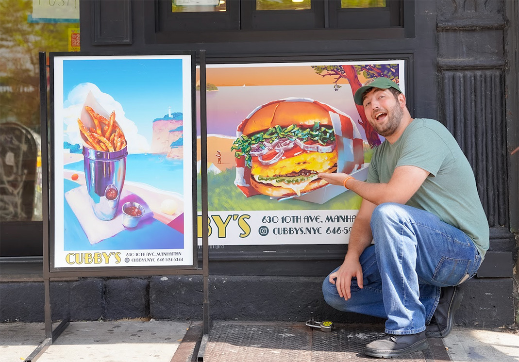 A man kneels beside a restaurant window displaying a large burger photograph