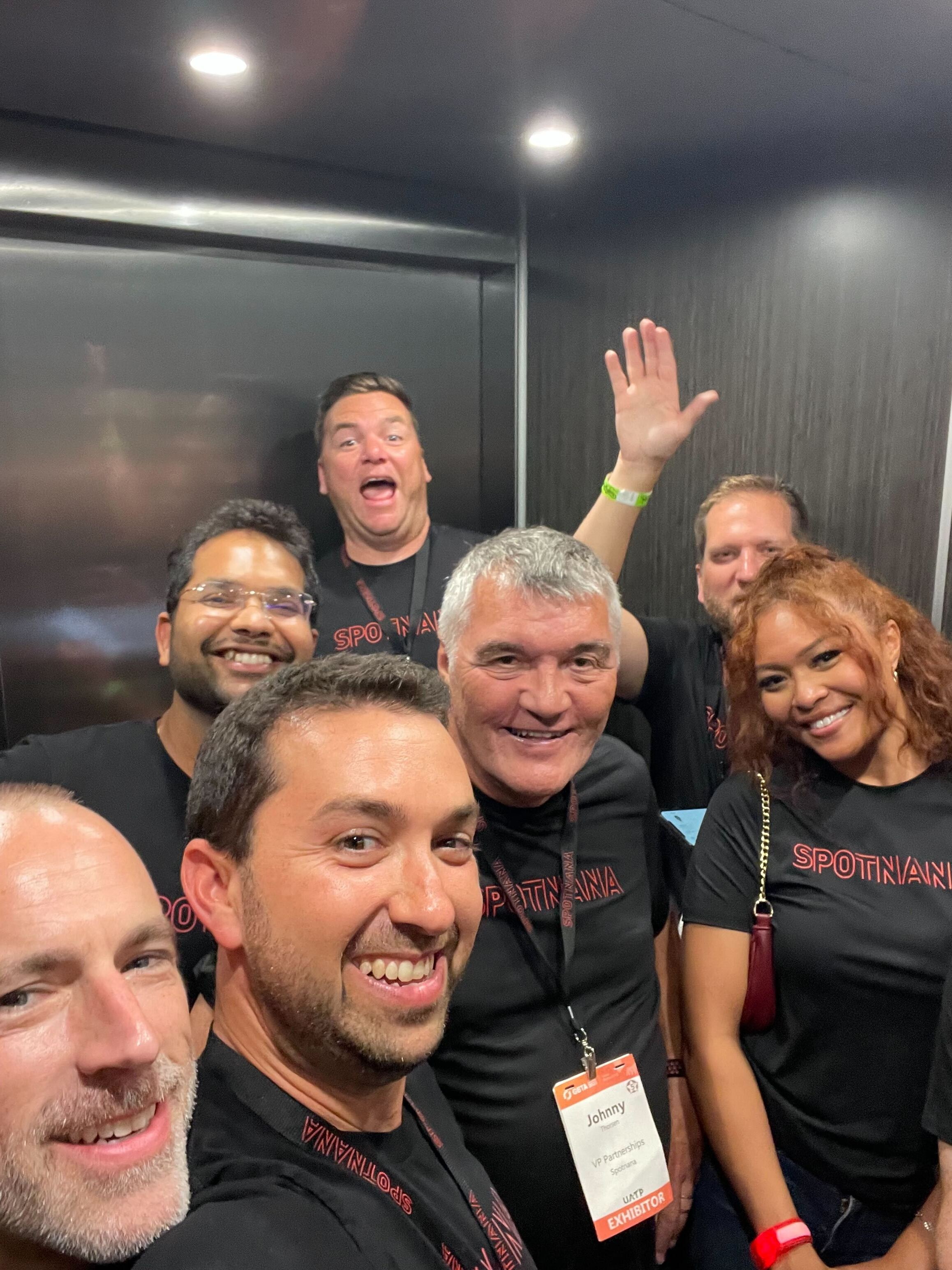 Spotnana colleagues wearing company shirts gather for a group selfie at a travel industry event