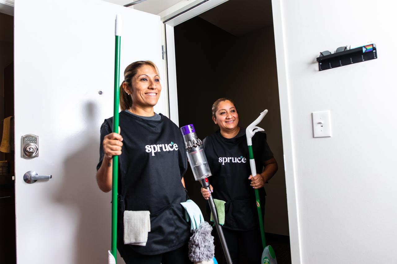 Two Spruce cleaning professionals entering an apartment with cleaning tools