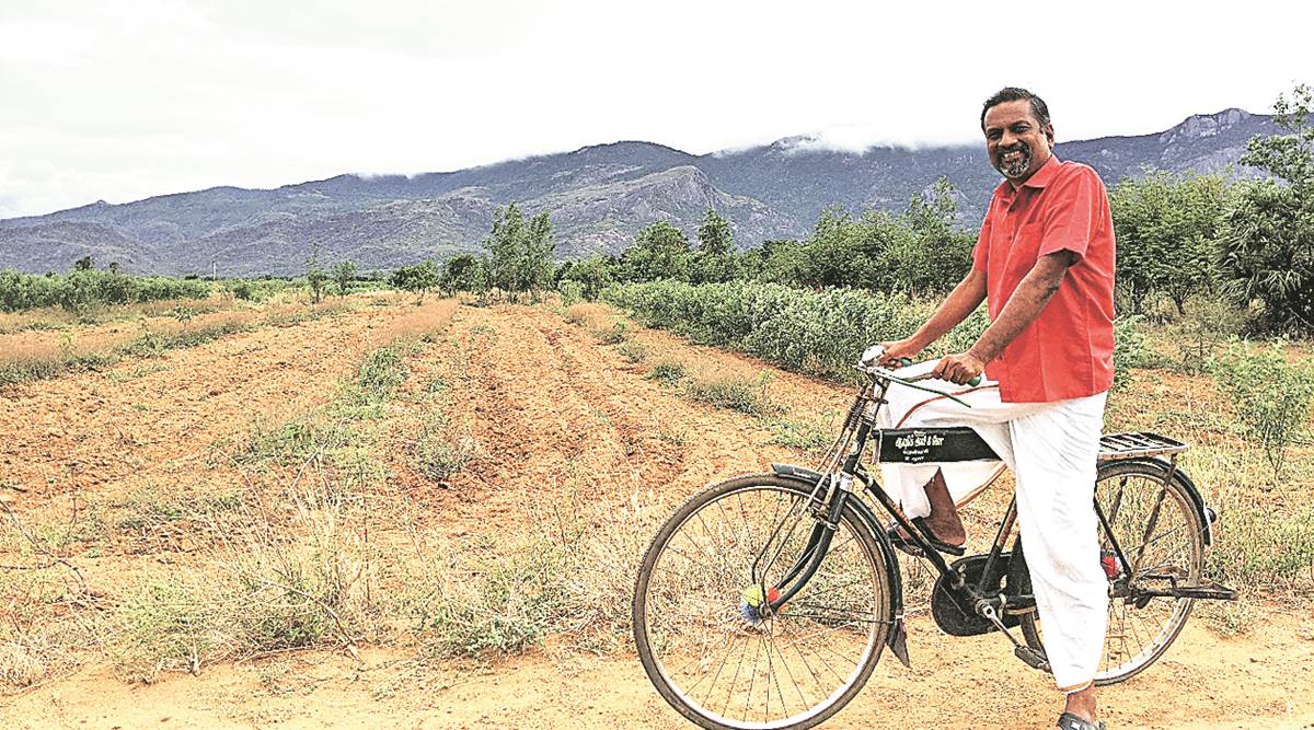 Sridhar Vembu beside a bicycle in a field near Tenkasi, with mountains behind him