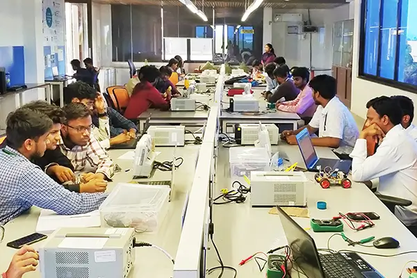 Participants working with laptops and electronics at benches in the SRiX IoT lab