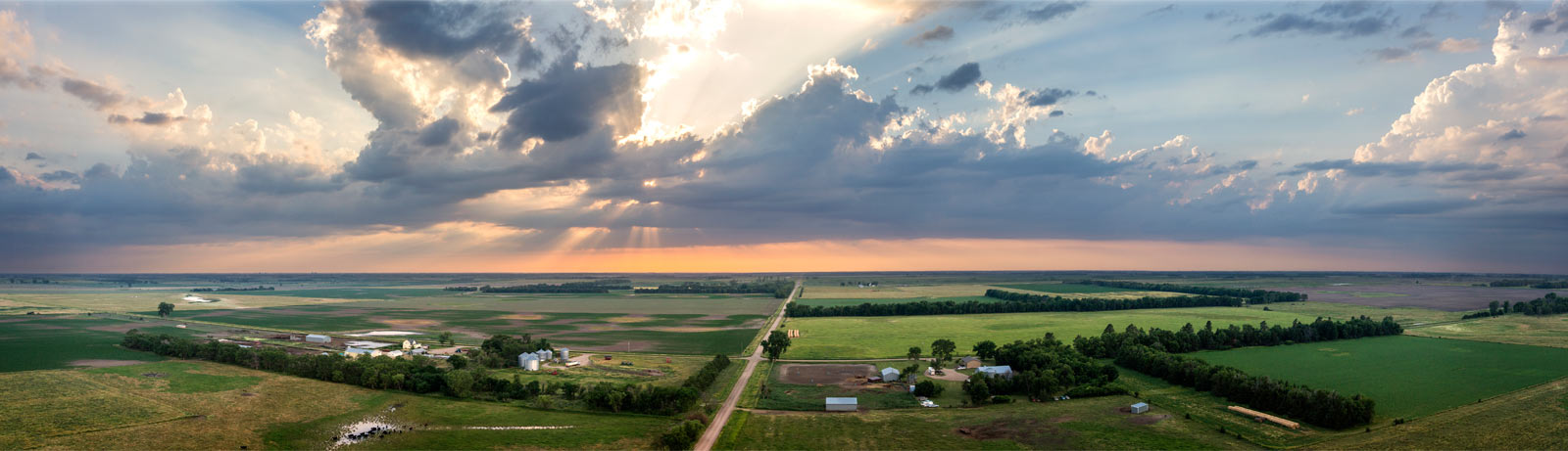 A road running through a wide rural landscape beneath a dramatic sky