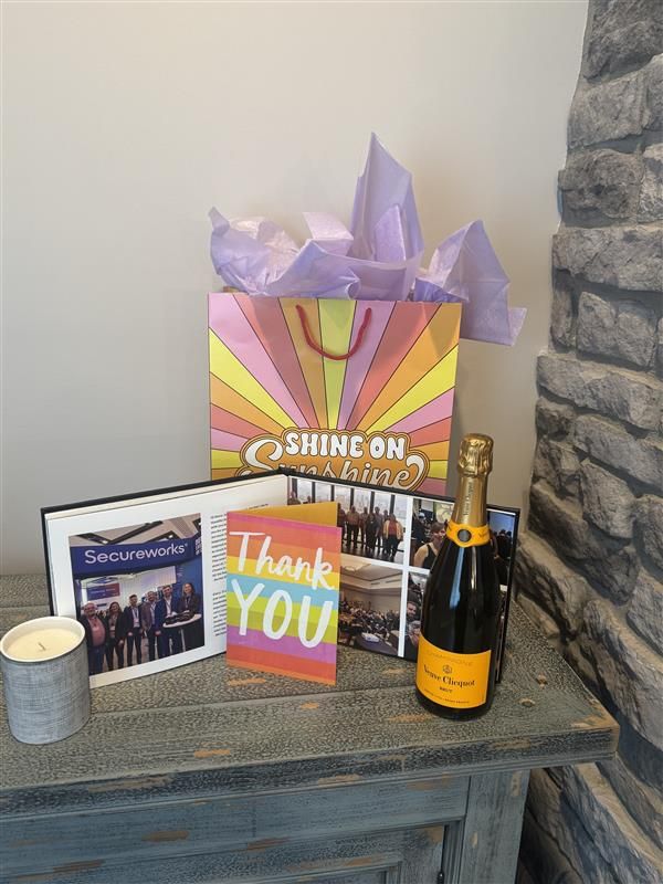 A Secureworks team memory book, thank-you card, gift bag and bottle arranged on a table