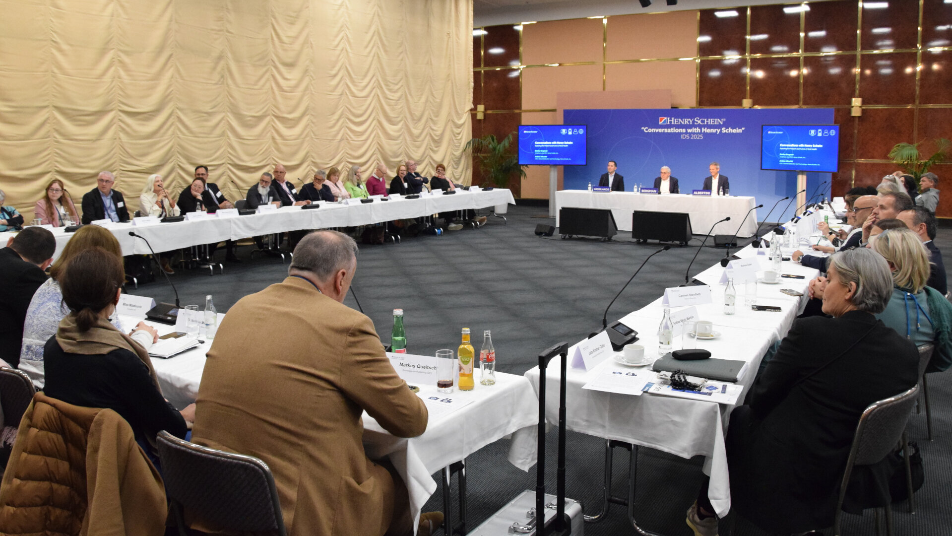 Stanley Bergman sits at the center of a three-person panel facing journalists at a media session in Cologne.