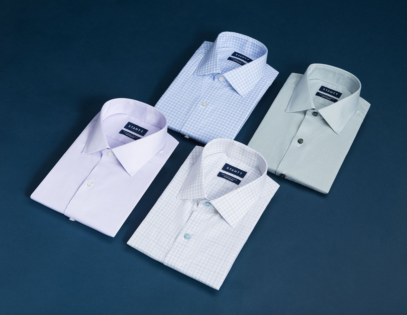 Four folded Stantt shirts in different checks and colors arranged on a navy surface