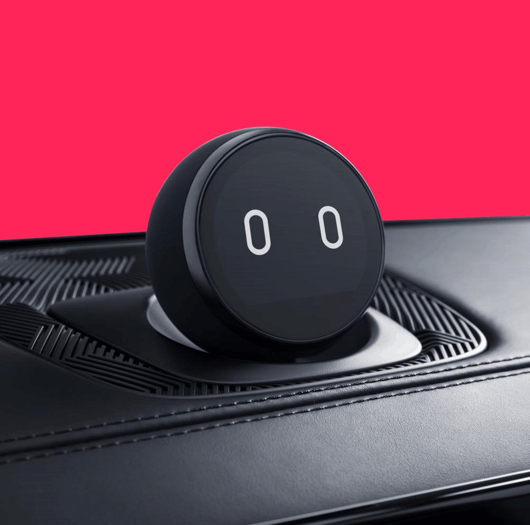 NIO’s round NOMI dashboard companion, with two illuminated eyes, against a vivid pink background