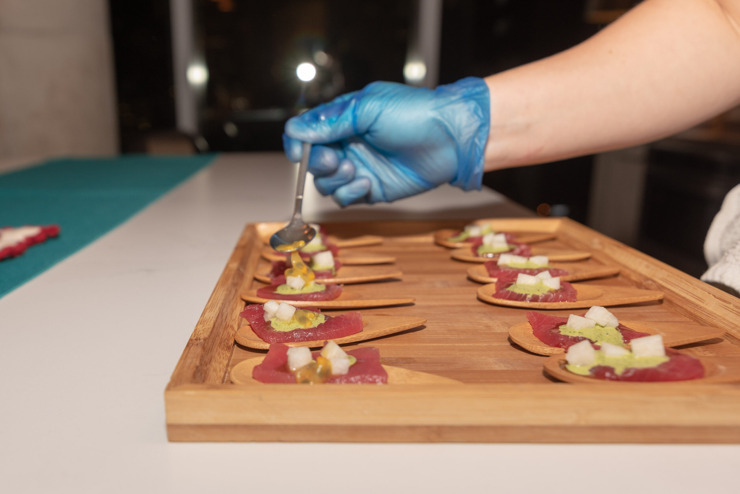 A gloved hand plates small bites for guests at a produced event