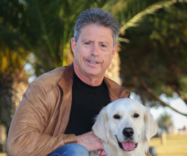 Eric Starkman kneeling beside his golden retriever, Ben, outdoors