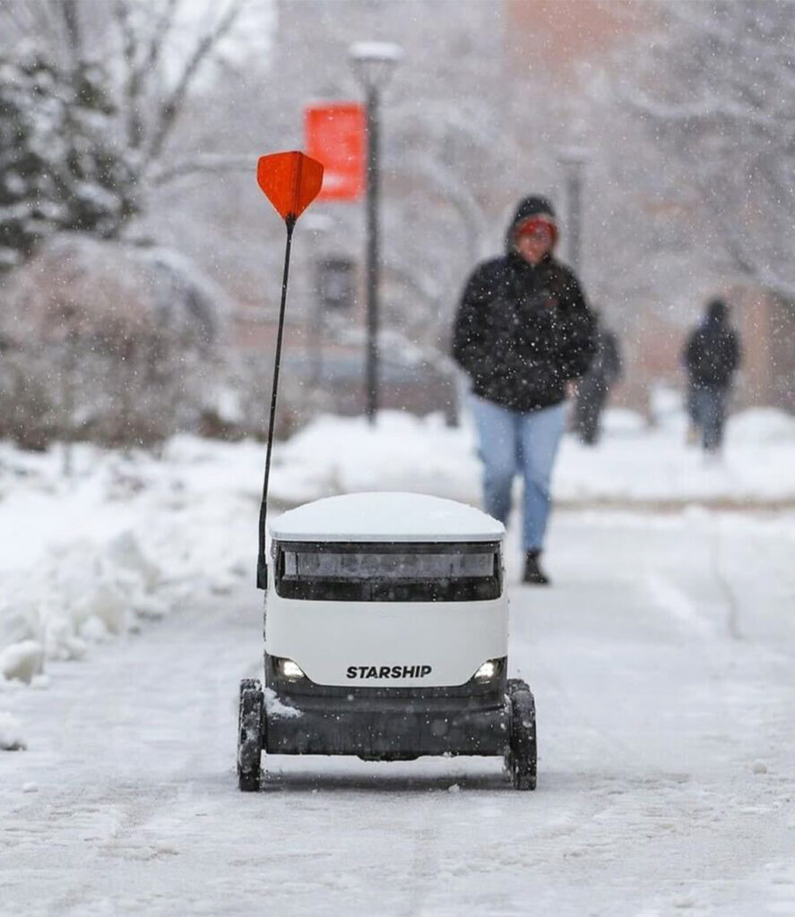A Starship delivery robot driving through falling snow