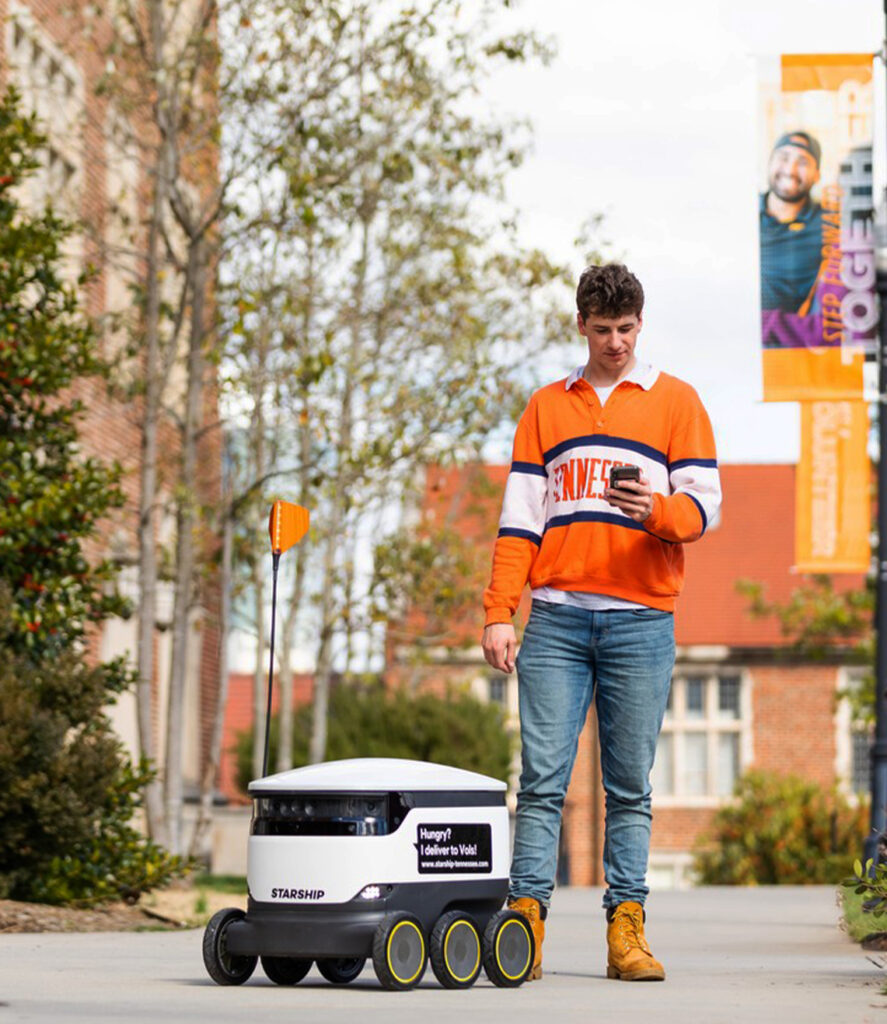A student walks beside a Starship robot on a university campus