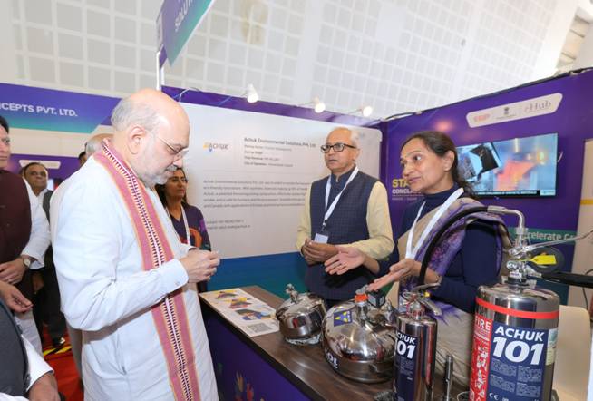 Amit Shah listens to an exhibitor beside stainless-steel equipment at Startup Conclave 2025