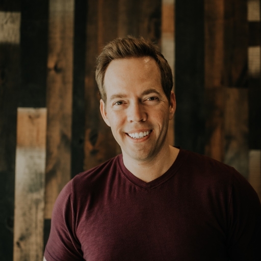 Startups.com founder and CEO Wil Schroter smiling in front of a wooden wall