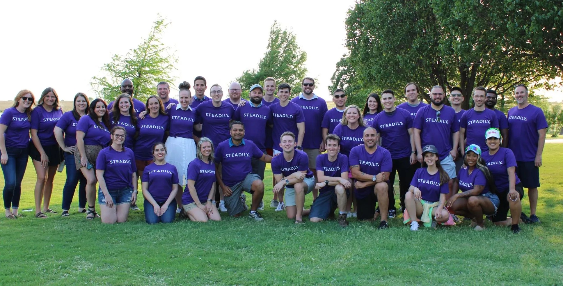 Steadily team gathered outdoors in purple company shirts
