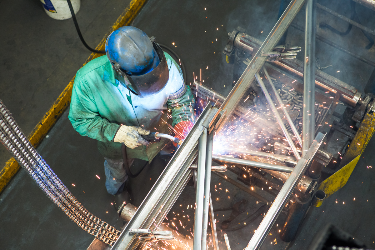 A worker in protective welding gear joins steel components, with sparks visible
