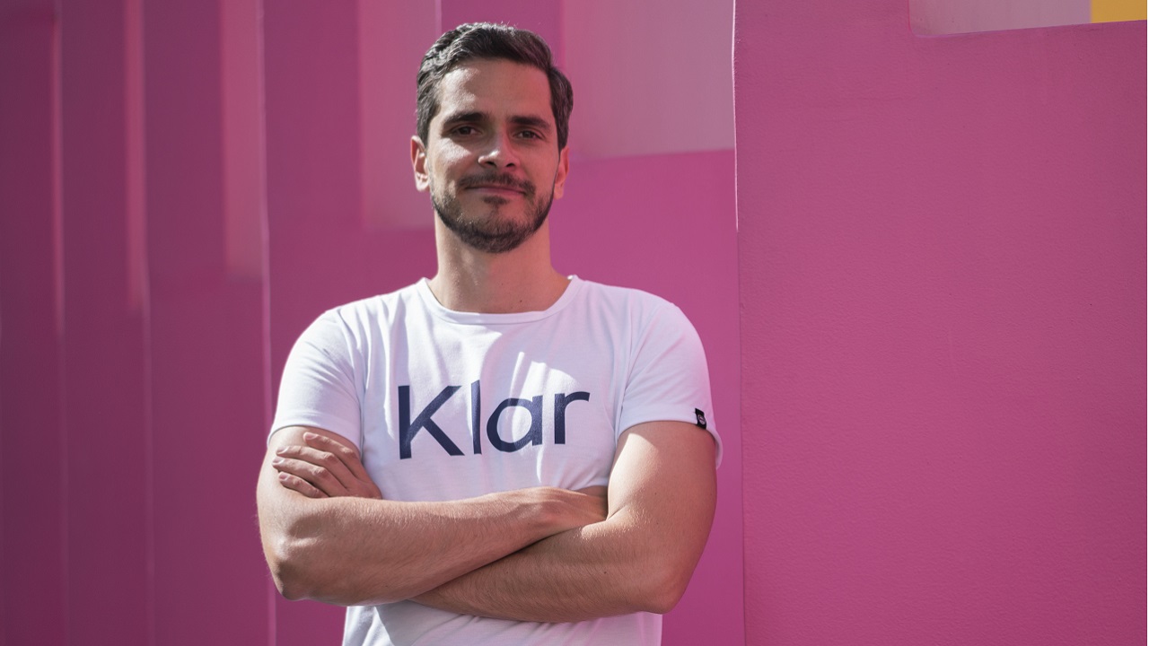 Stefan Möller wearing a white Klar T-shirt against a pink wall