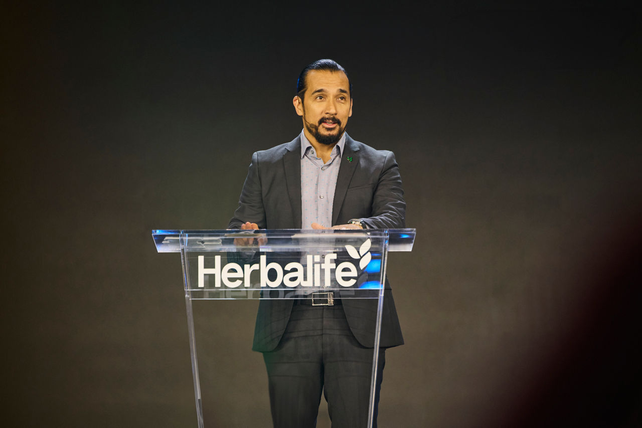 Stephan Gratziani speaking from a transparent Herbalife lectern at Honors 2025 in Los Angeles