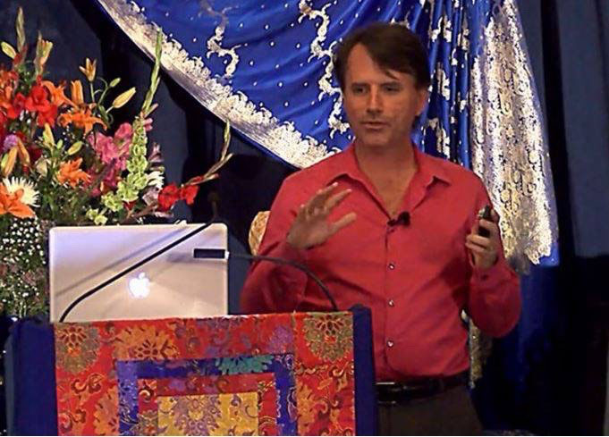 Stephen Dinan speaking beside a laptop at the Seven Rays Conference