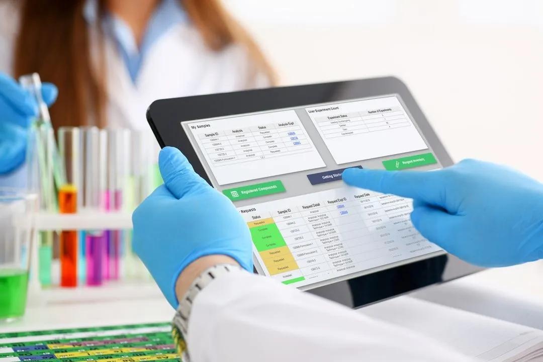 A laboratory worker uses Dotmatics software on a tablet beside a rack of colourful test tubes