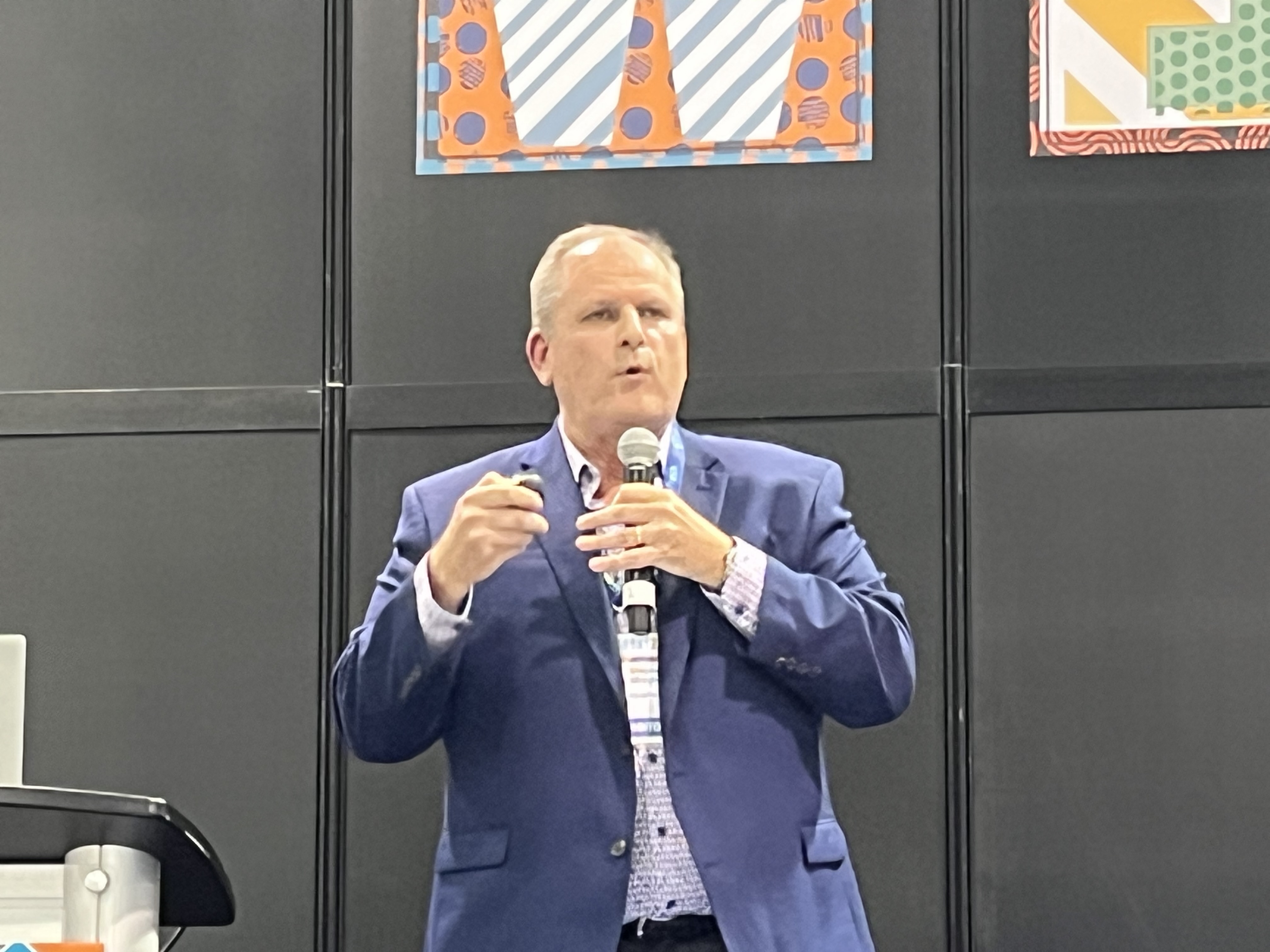Stephen Midgley speaking with a handheld microphone at the 2023 IDDBA Expo