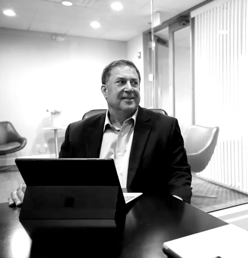 Stephen Pope seated at a meeting table with a computer, looking toward someone outside the frame
