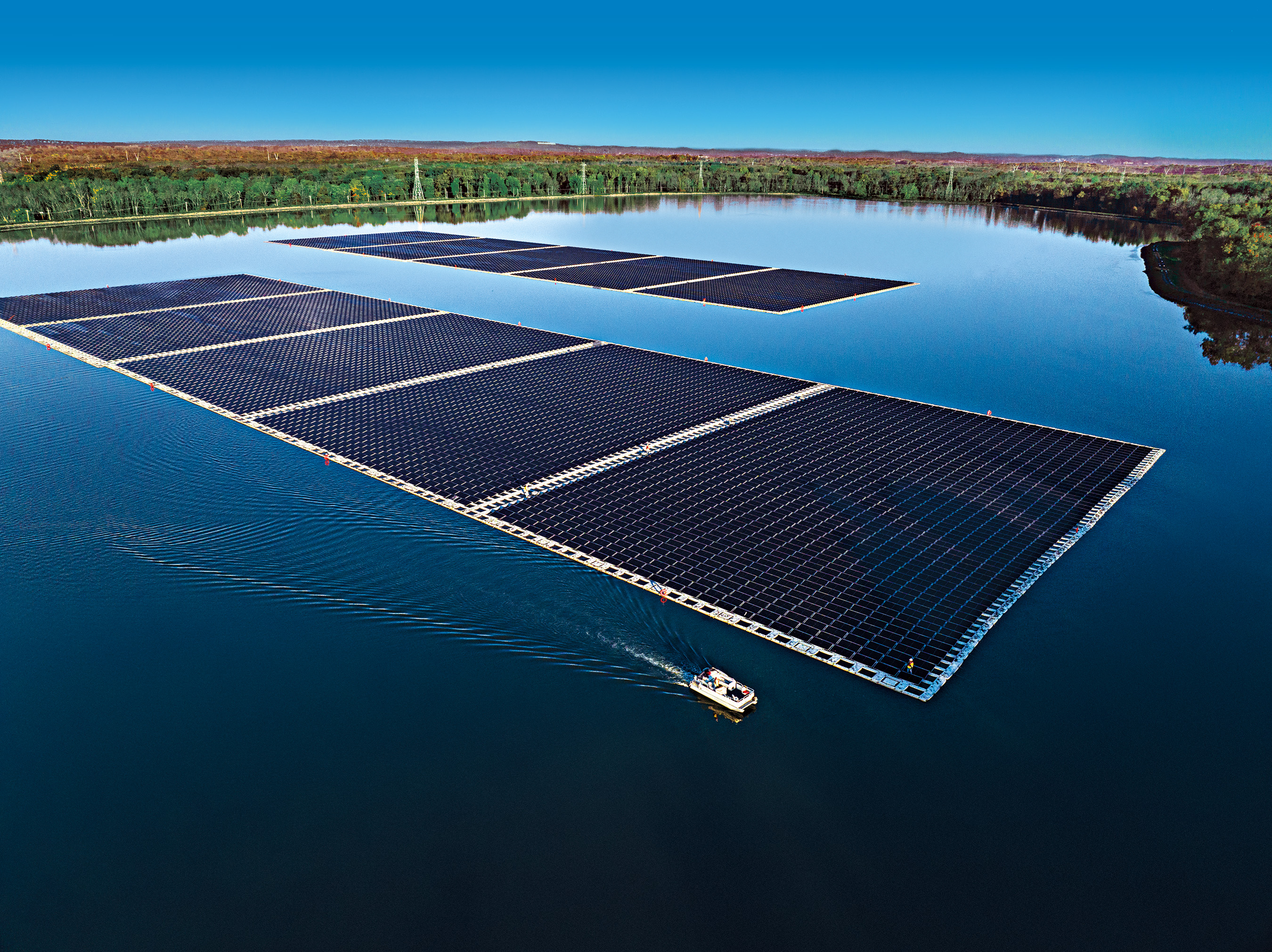 Aerial photograph of the Canoe Brook reservoir with rows of floating solar panels surrounded by trees