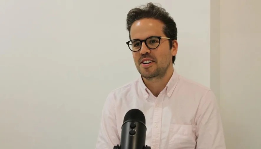 Stephen Whitworth wearing glasses and a pale shirt, seated behind a microphone during his Ravelin years
