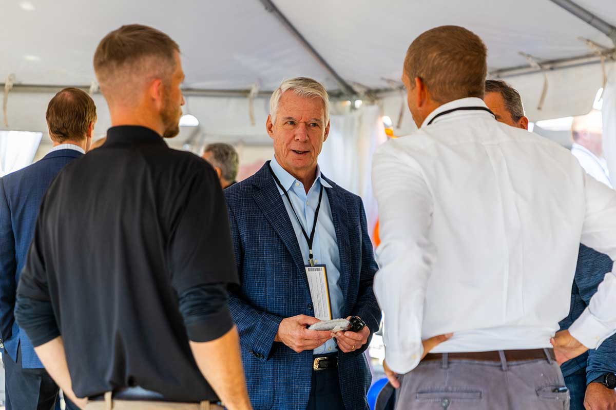 Steve Angel in a blue jacket speaking with two men at an event.